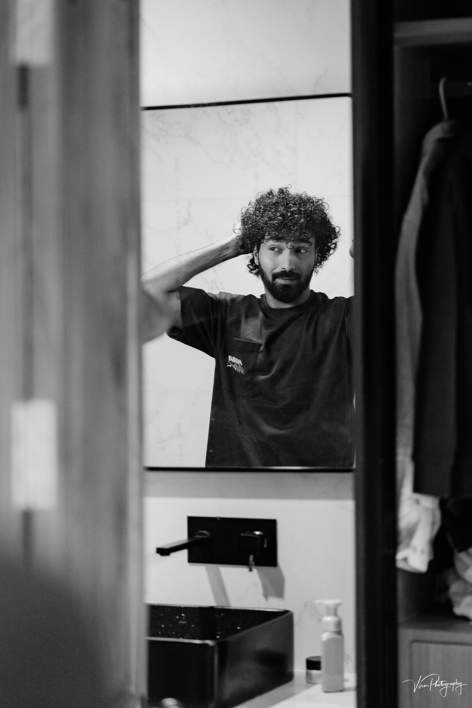 Black and white mirror reflection of person with curly hair making surprised expression in bathroom.