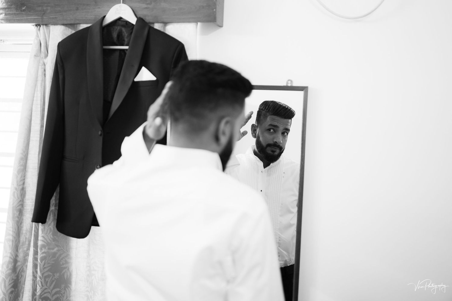 Black and white photo showing a reflection in a mirror with a dark blazer hanging on the wall.