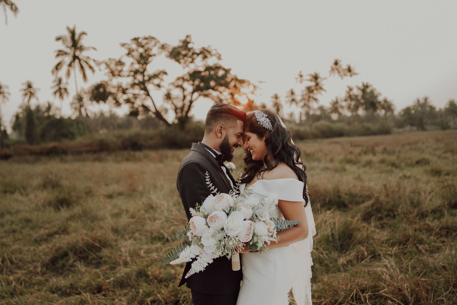 An intimate wedding moment captured in a field with palm trees at golden hour.