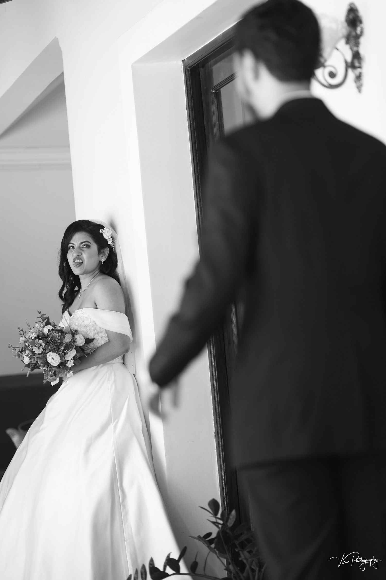 Black and white wedding photograph capturing an intimate first look moment between a bride in a flowing gown and groom near a doorway.