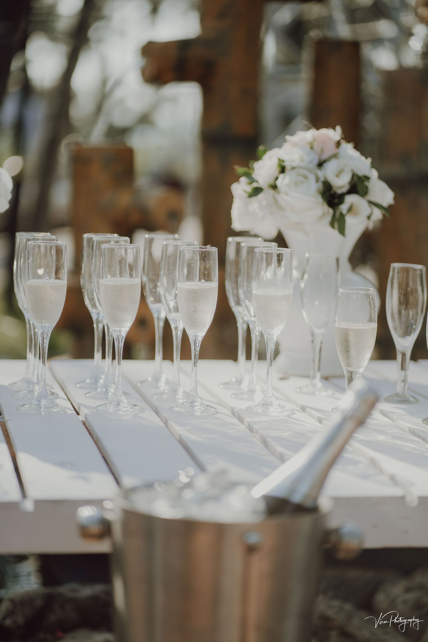 Elegant champagne flutes and wine glasses arranged on white tablecloth with floral centerpiece and silver ice bucket.