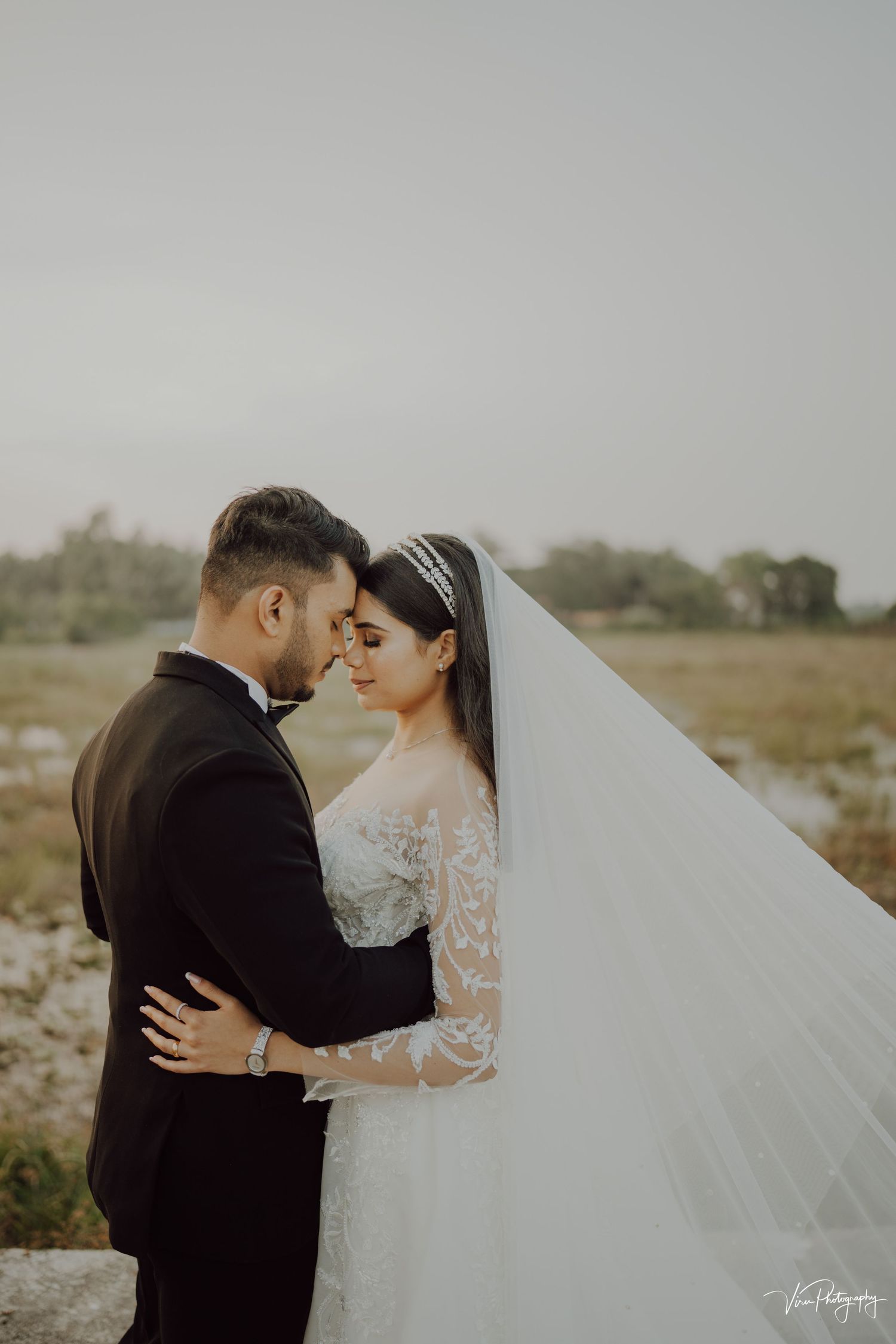 Romantic wedding portrait of a couple embracing in a dreamy outdoor setting with flowing white veil against natural scenery.