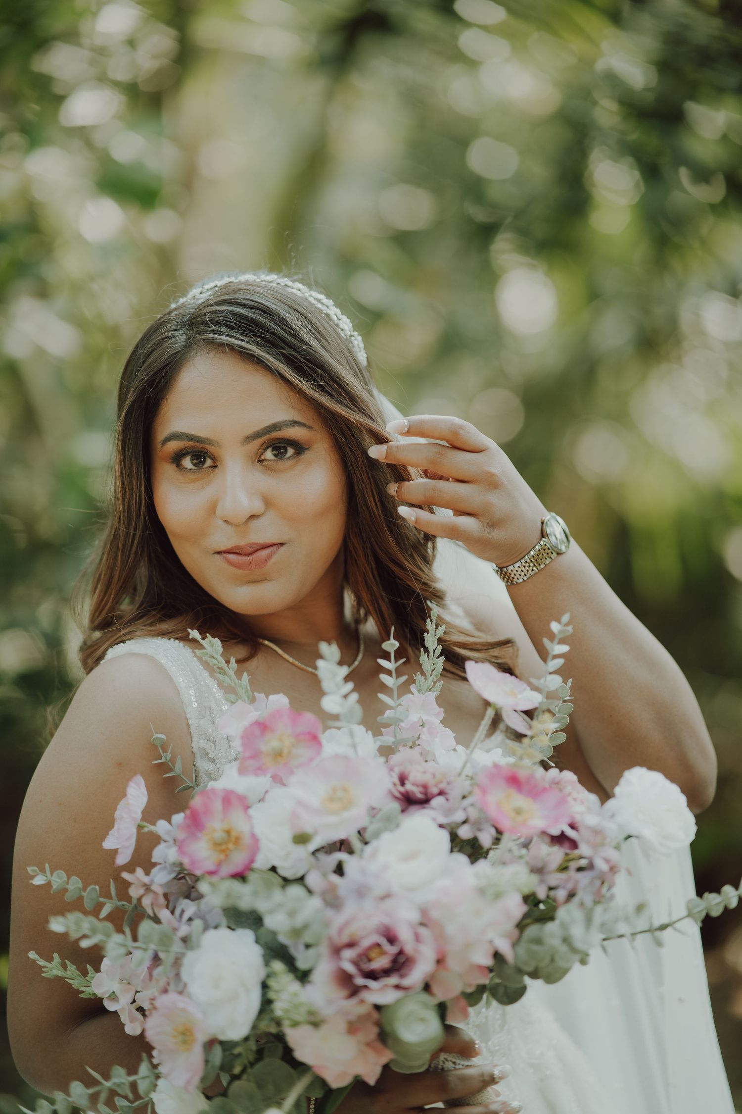 A bride in a white dress holds a beautiful bouquet of pink and white flowers against a soft bokeh background.