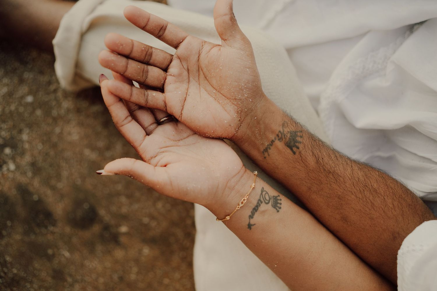 Close up of two hands with small minimalist tattoos holding each other against a white fabric background.