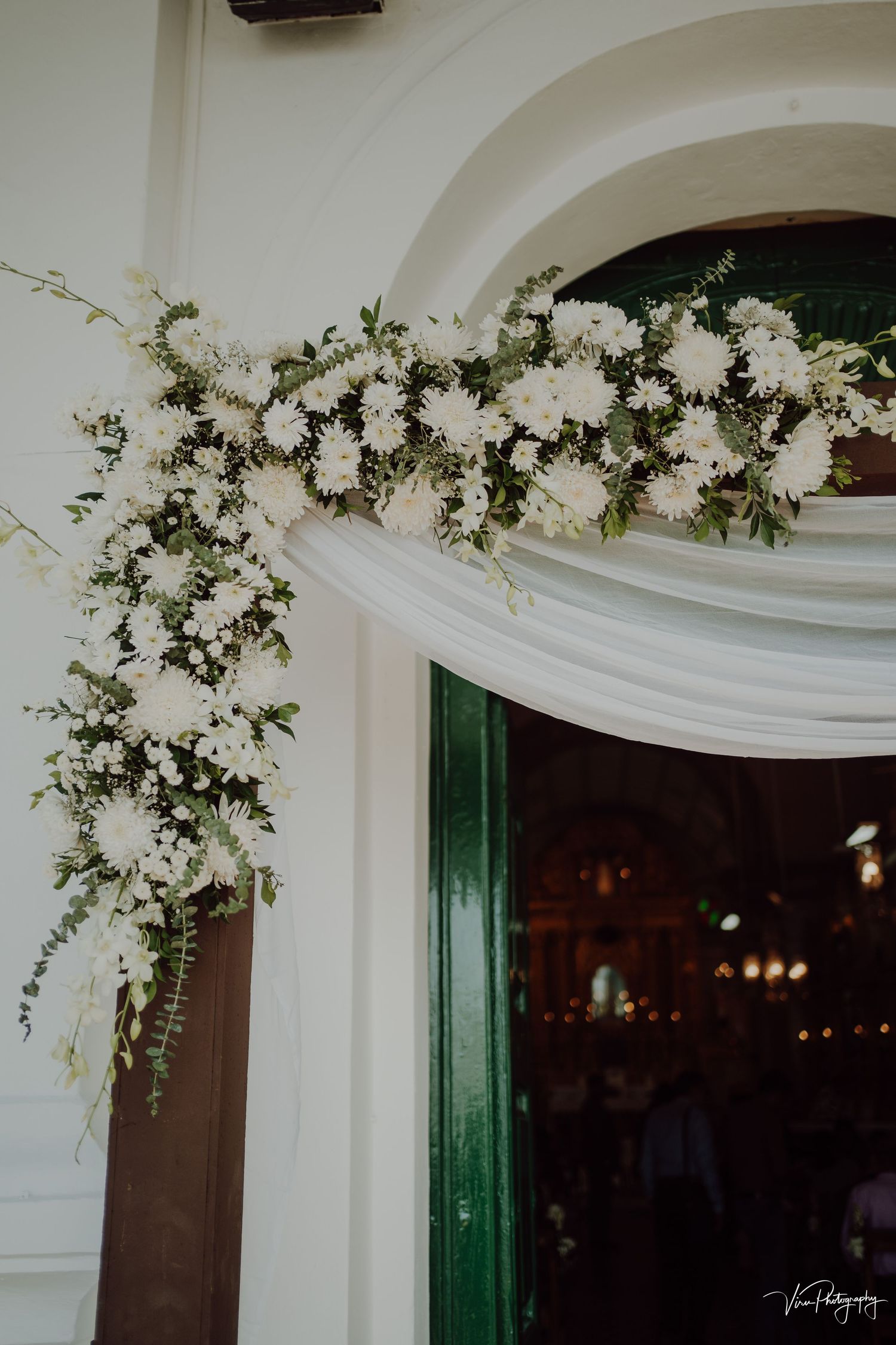 Elegant white floral arrangements and greenery decorate an arched doorway entrance with emerald green details.