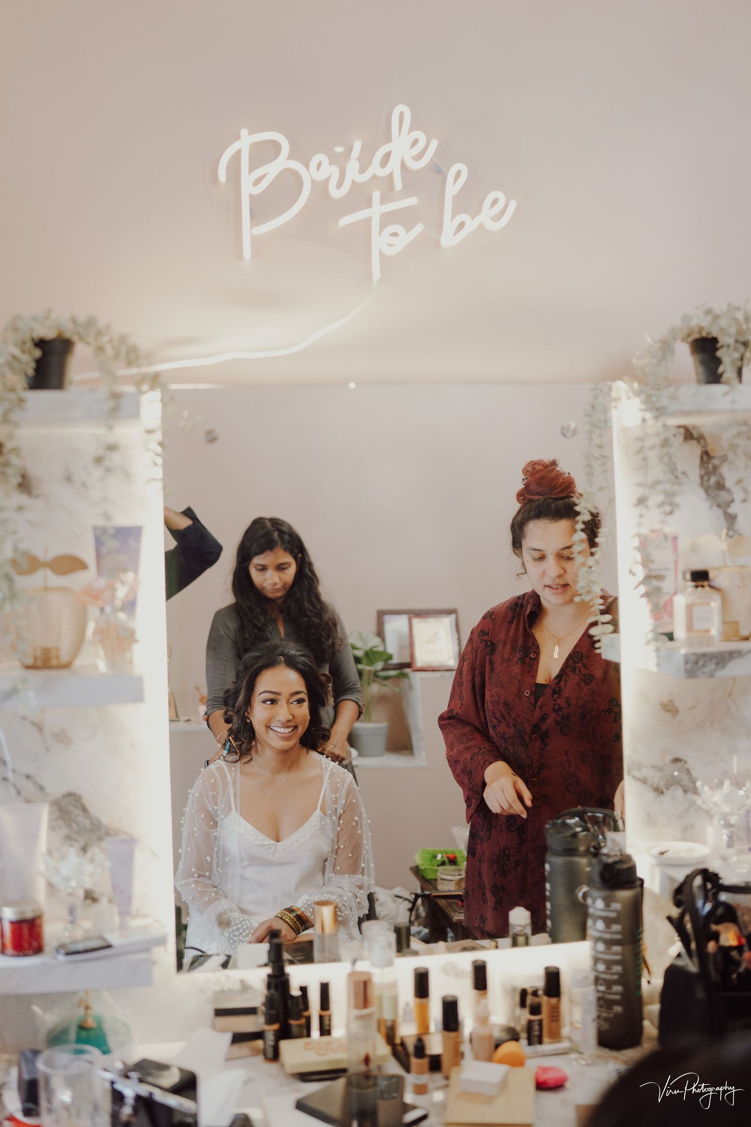 Wedding preparations scene with a neon 'Bride to be' sign and beauty products on a table in a stylish bridal room.