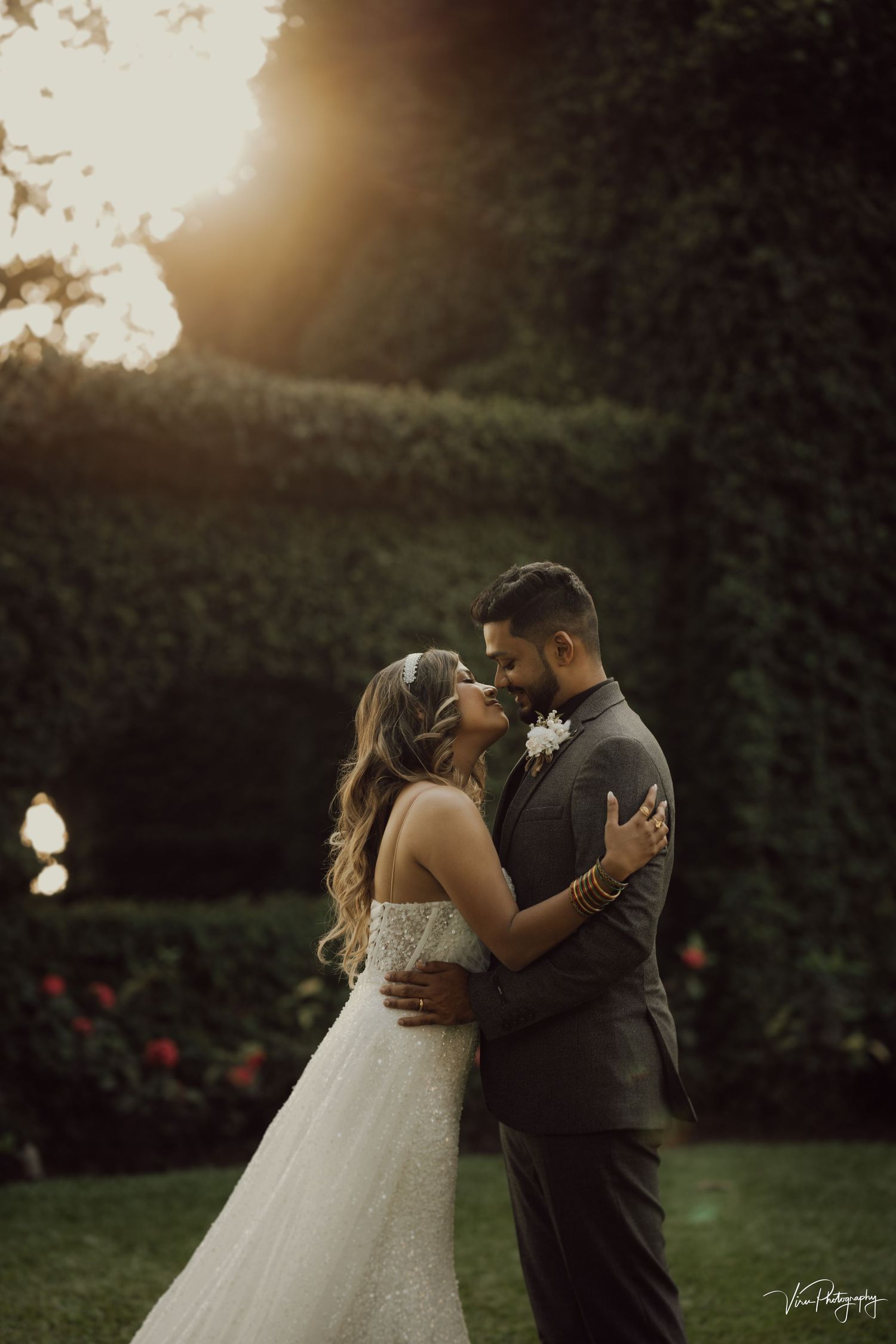 A couple shares an intimate moment at sunset in a garden setting with beautiful golden hour lighting.