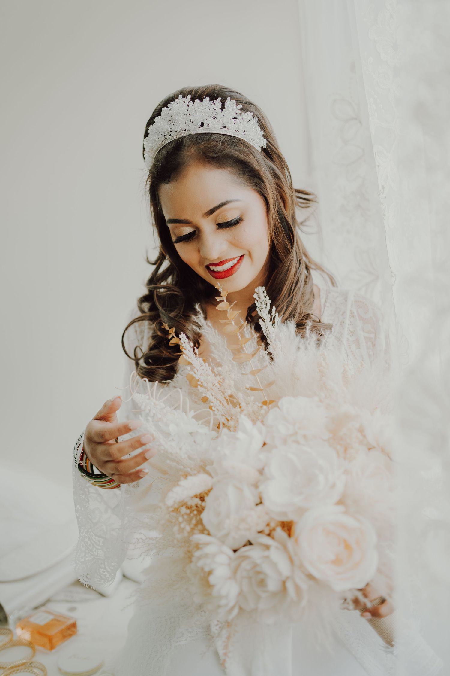 Beautiful bride in white dress with intricate beaded headpiece smiles while holding a romantic blush and cream floral bouquet.