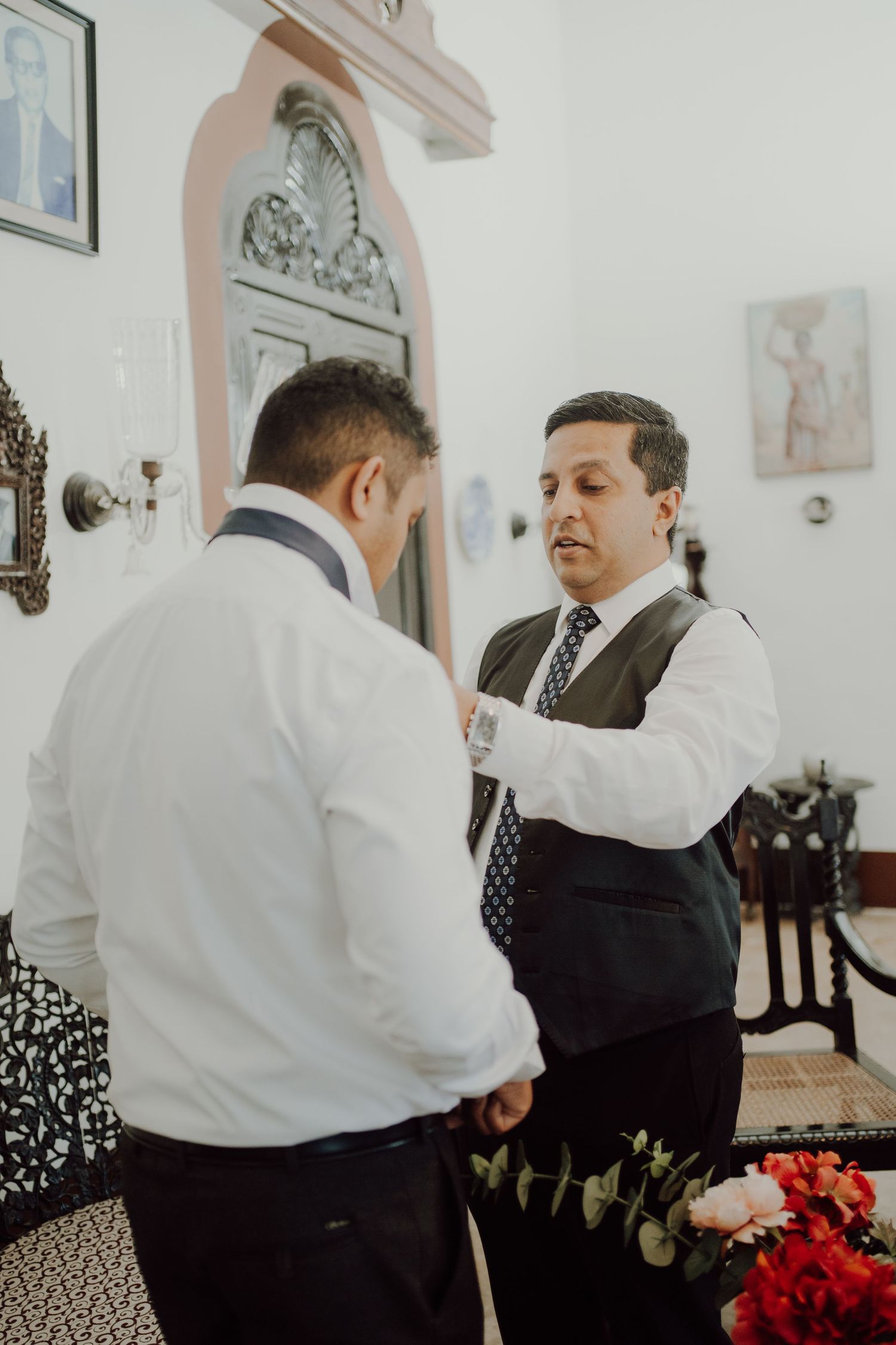 Two men in formal attire adjusting their wedding day outfits in an ornate room.