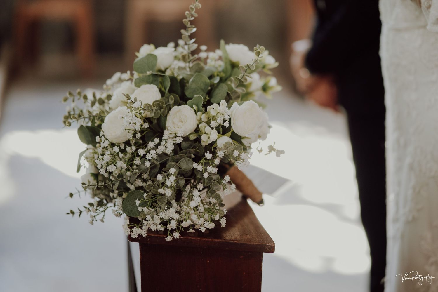White wedding bouquet with roses and baby's breath flowers sits on wooden stand during ceremony.