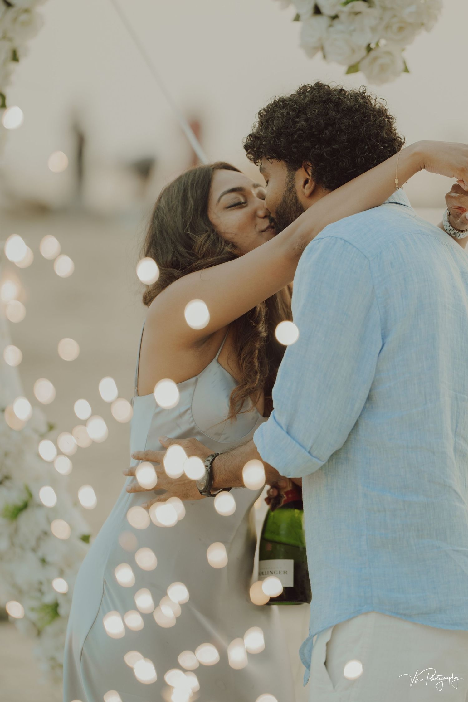 A romantic couple embraces while dancing outdoors with ethereal bokeh lights sparkling in the foreground.