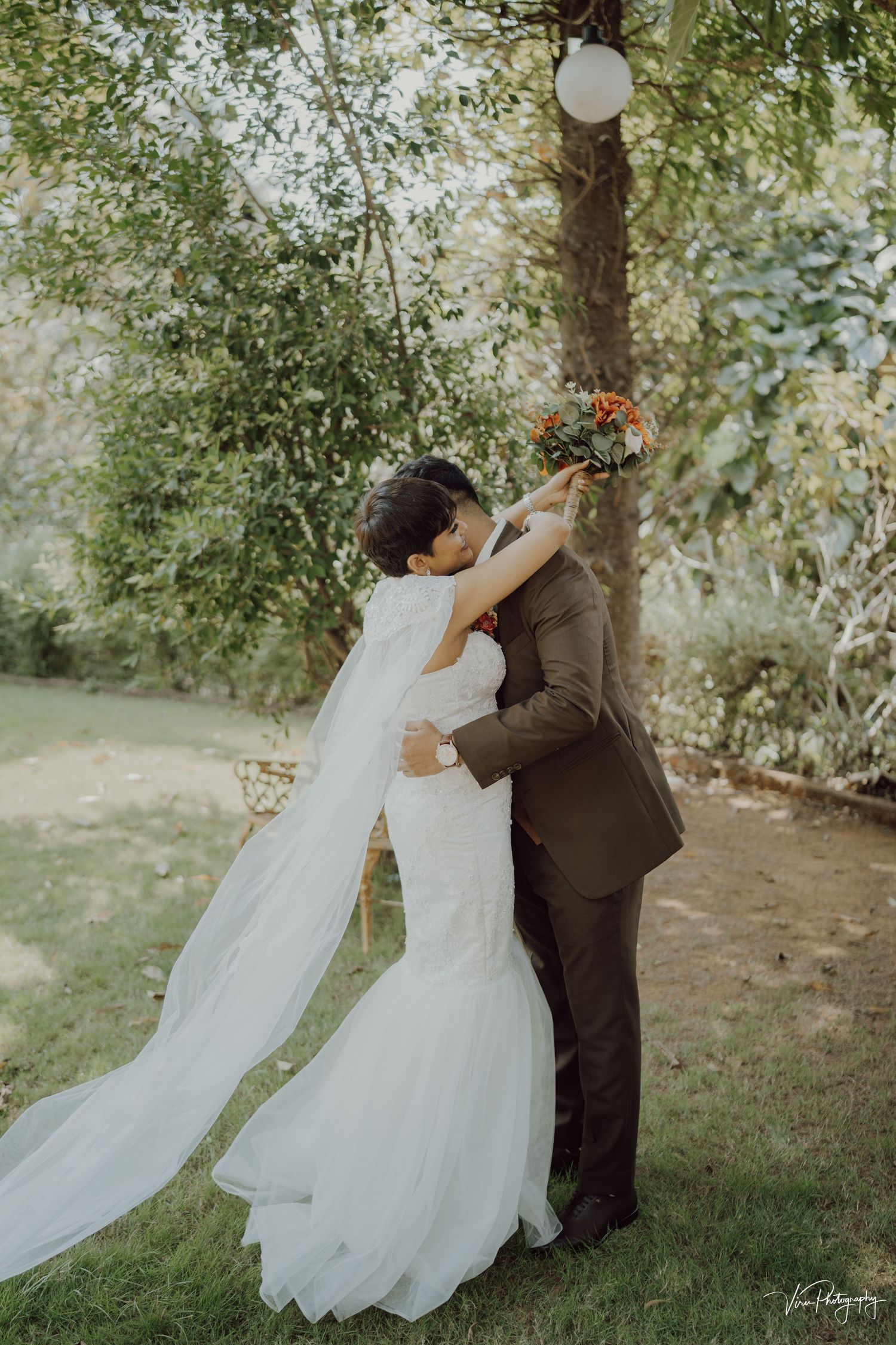 A romantic dance pose sequence between a couple in wedding attire under trees, with a flowing white veil in motion.