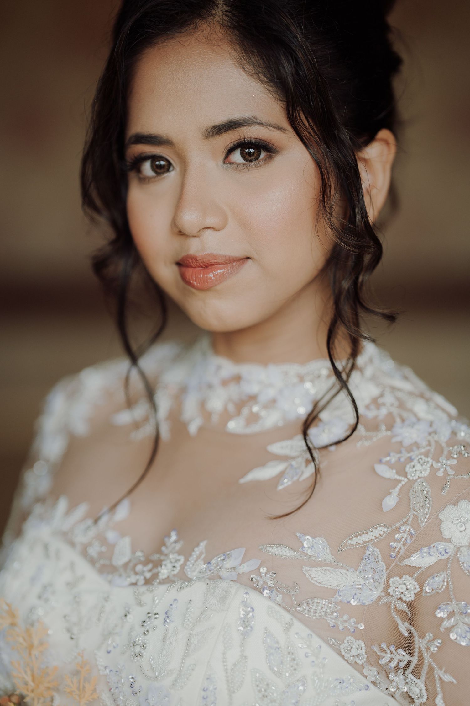 Smiling bride with an elegant updo and soft makeup wearing a white gown with sheer floral lace sleeves.