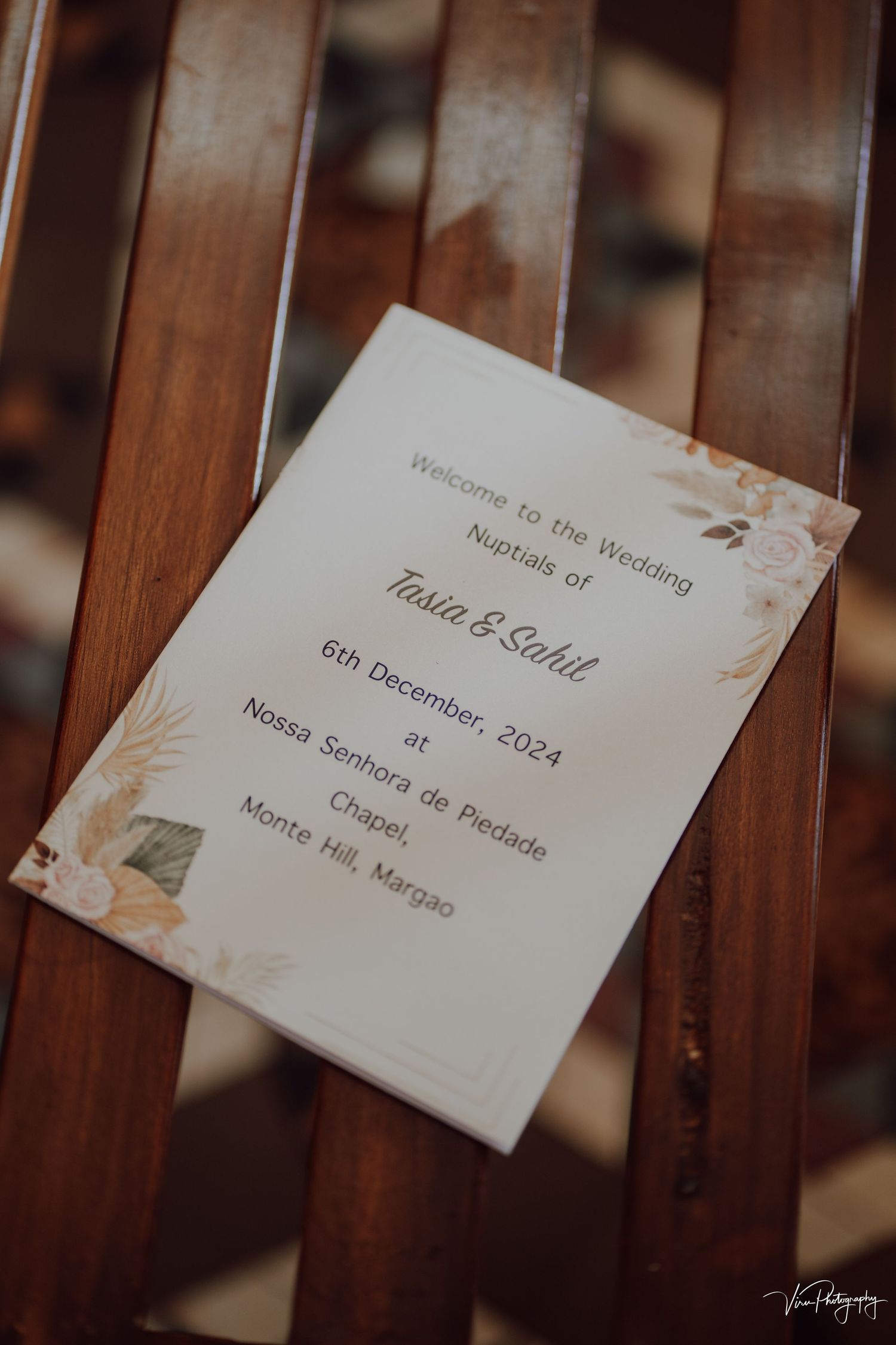 Wedding invitation card resting on wooden slats shows details for Paula and Saad's December 2024 ceremony.