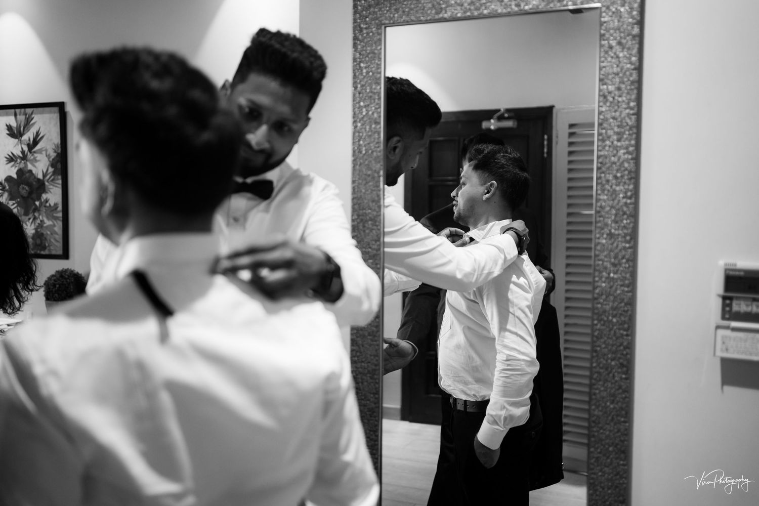 A black and white image showing people getting dressed and making final adjustments in front of a mirror.