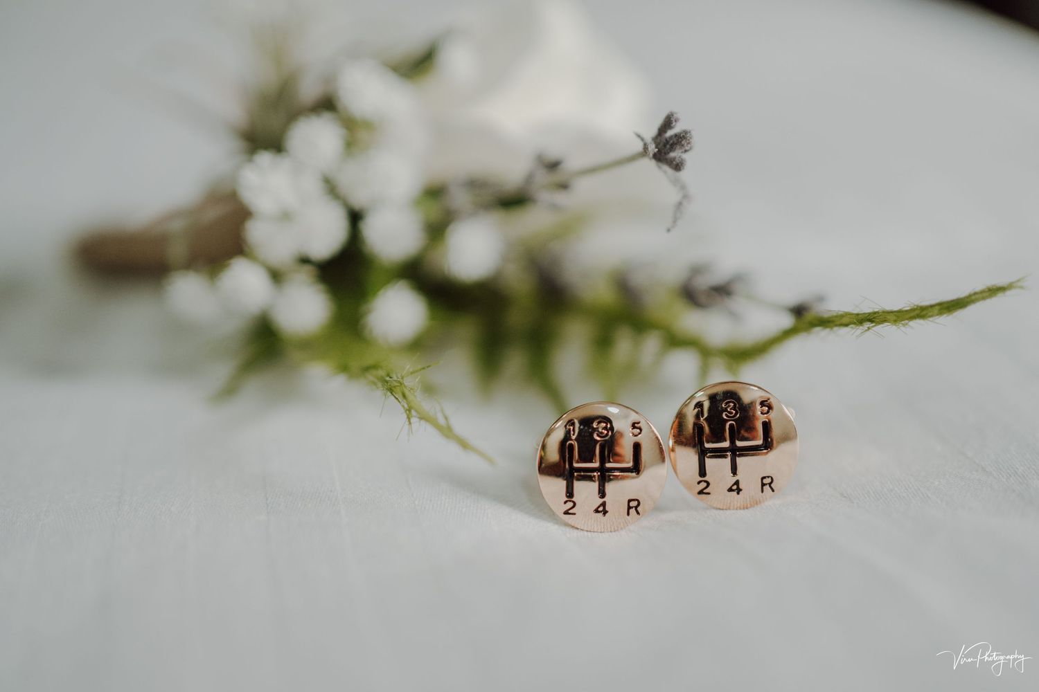 A pair of rose gold wedding rings rest on a white surface with delicate white flowers in soft focus background.