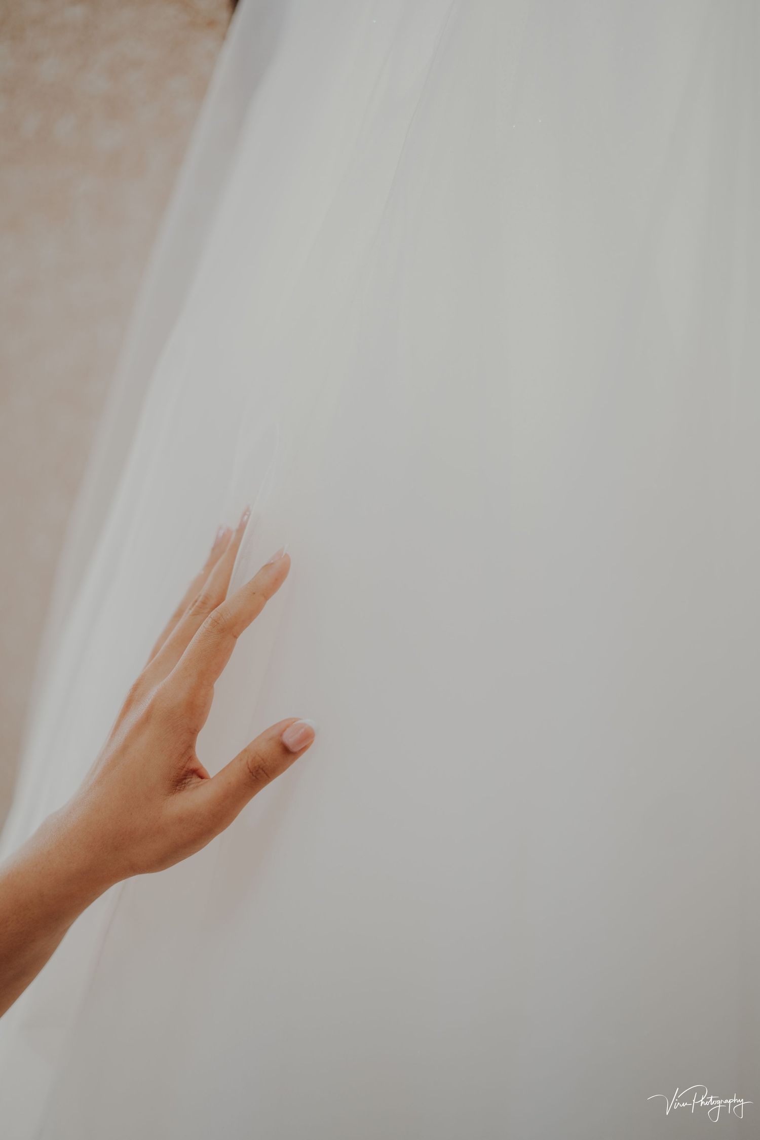 A delicate hand reaches out to touch sheer white fabric in a soft, ethereal composition.