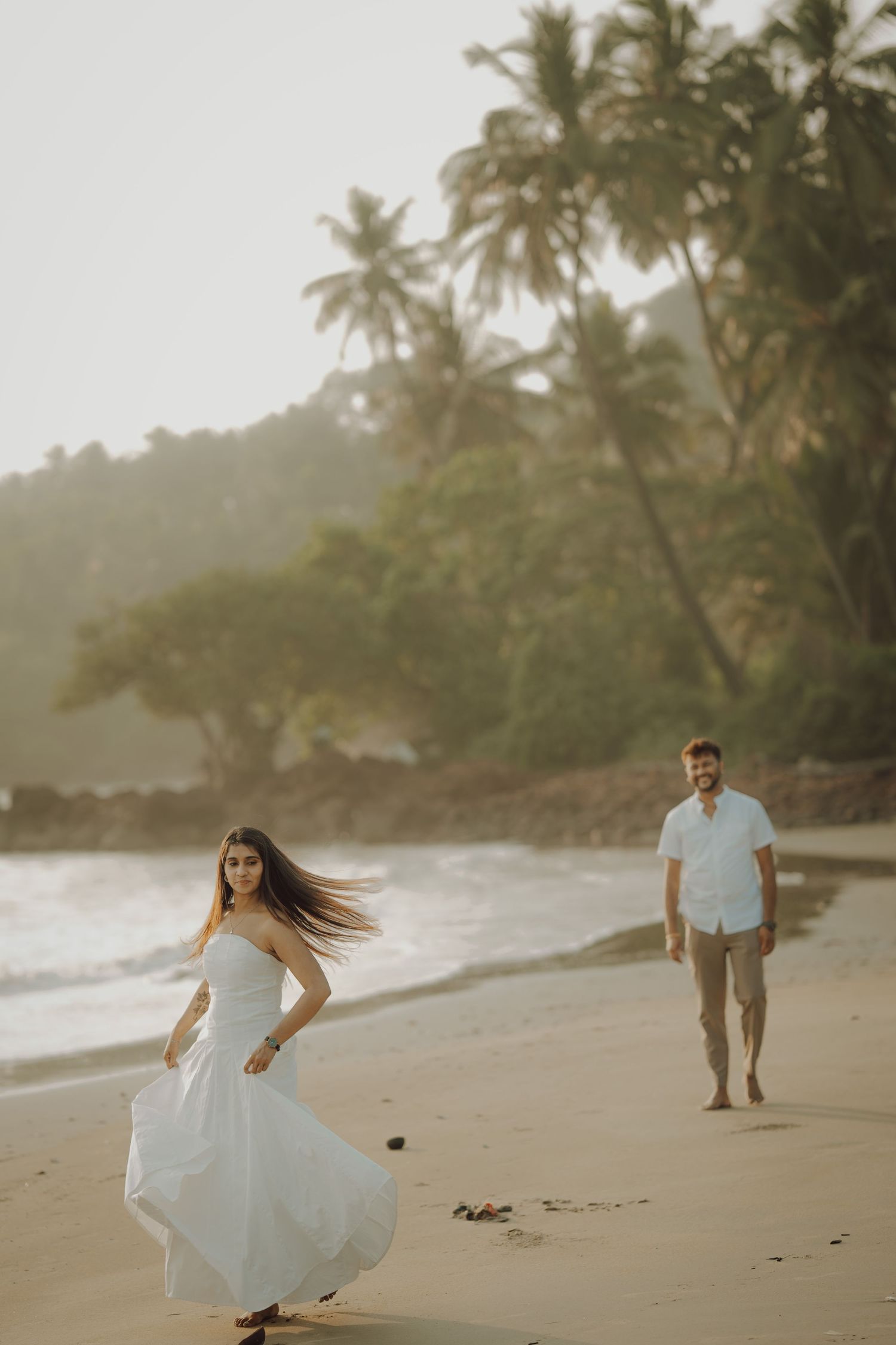 A couple walks along a tropical beach with palm trees at sunset creating a romantic silhouette against the ocean.