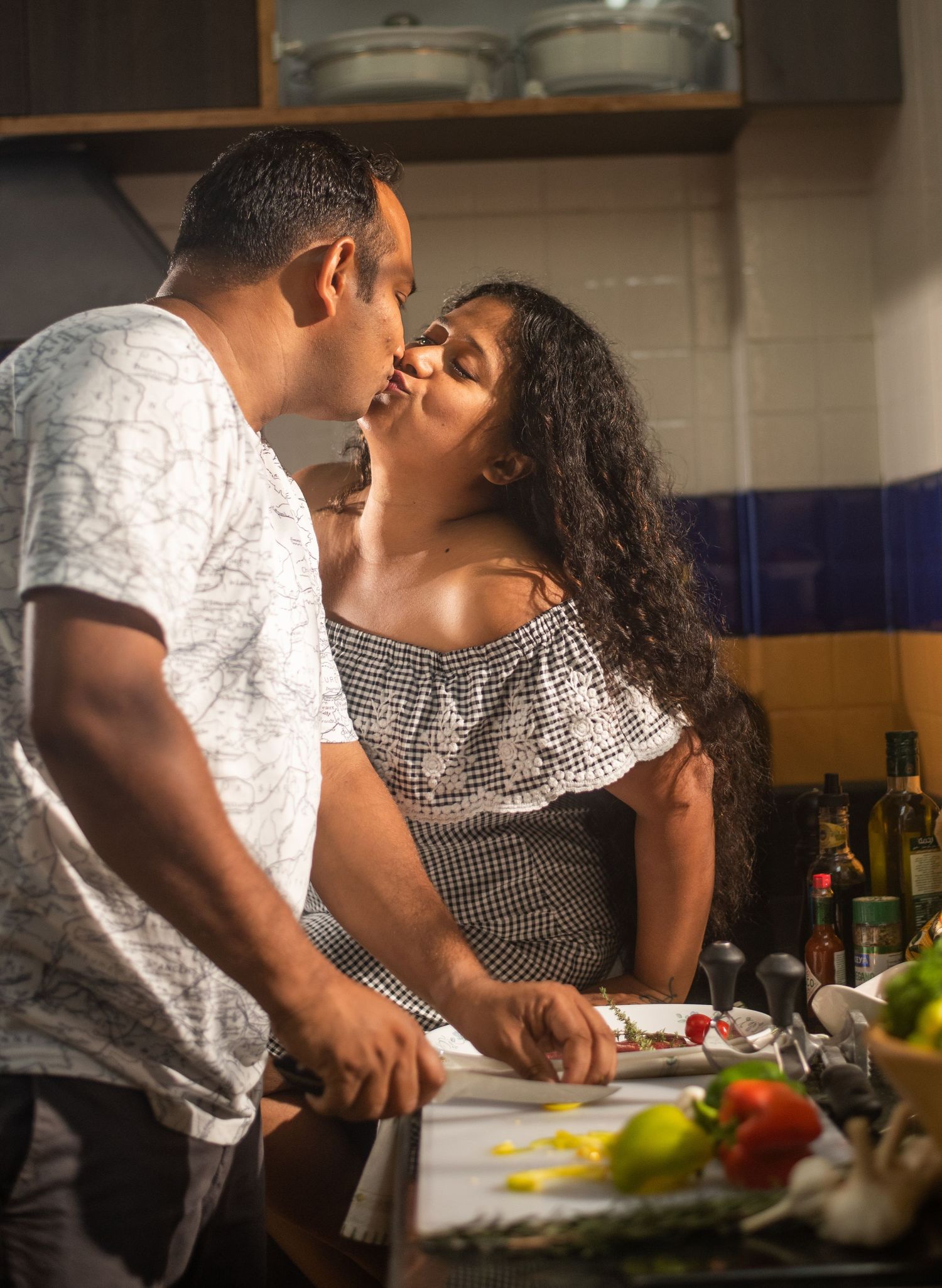 A couple shares an intimate moment while preparing food together in their kitchen.