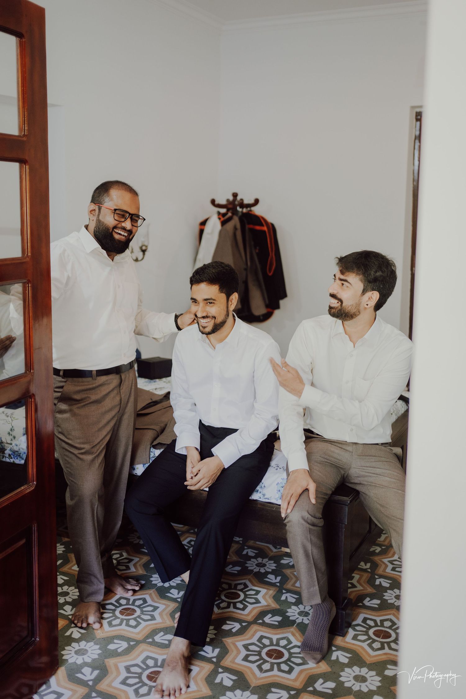 Three friends in white dress shirts share a candid laugh together while seated in a room with decorative tiled floors.