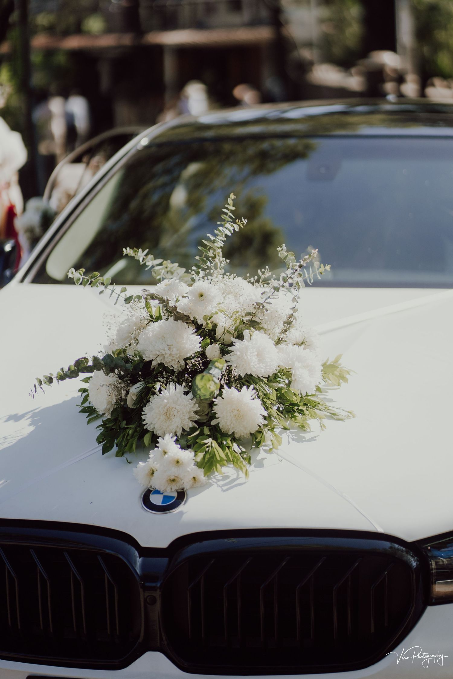 White floral wedding arrangement decorating the hood of a BMW car with its distinctive grille visible in the foreground.