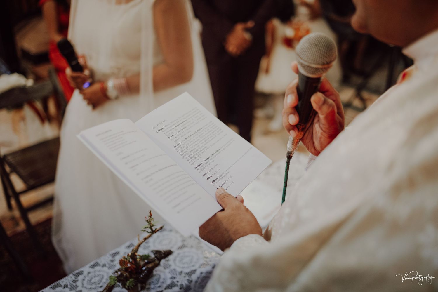 Close-up view of hands holding paper at a wedding ceremony while someone holds a microphone.