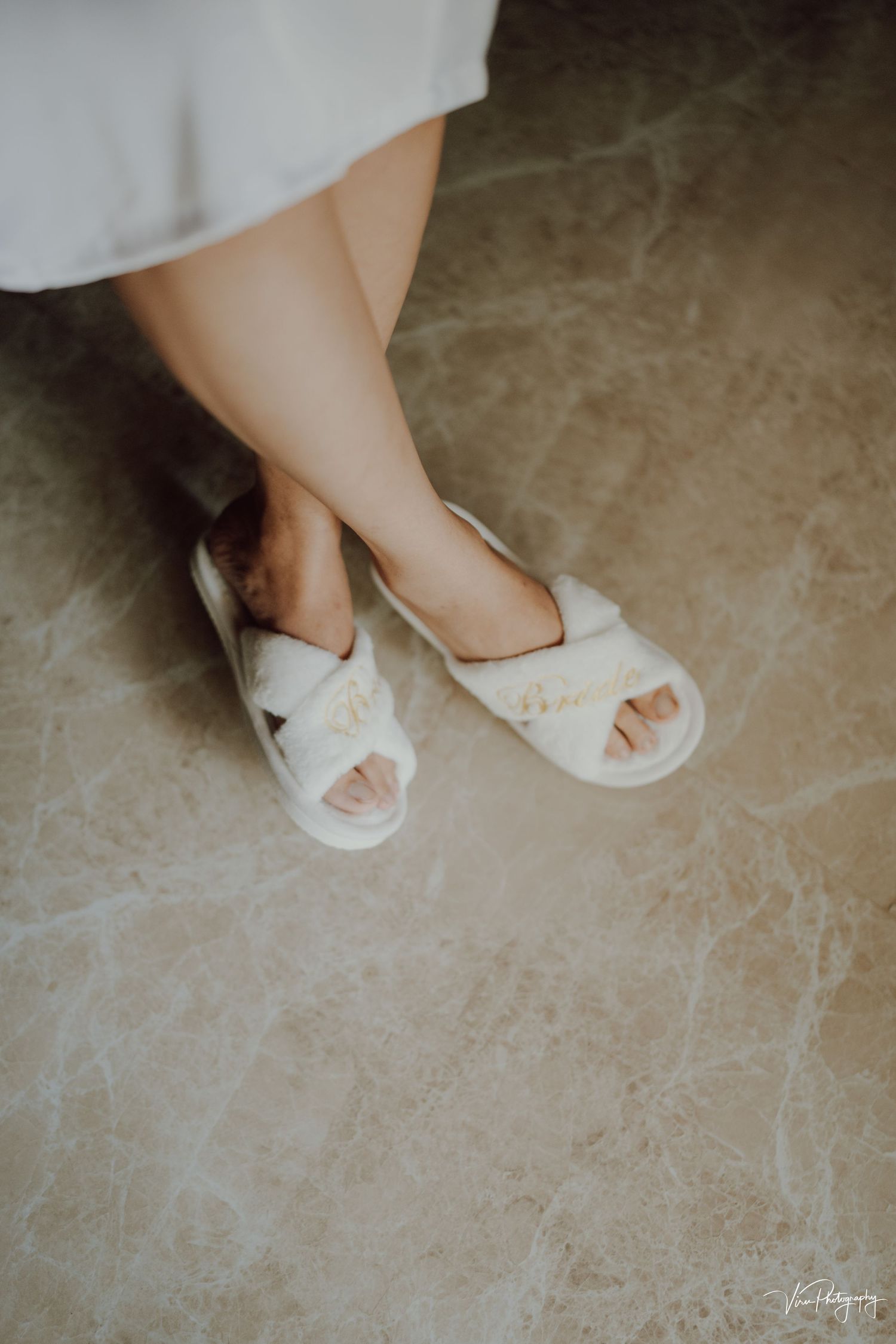 Woman wearing comfortable white plush slippers with quilted fabric and open toe design on marble floor.