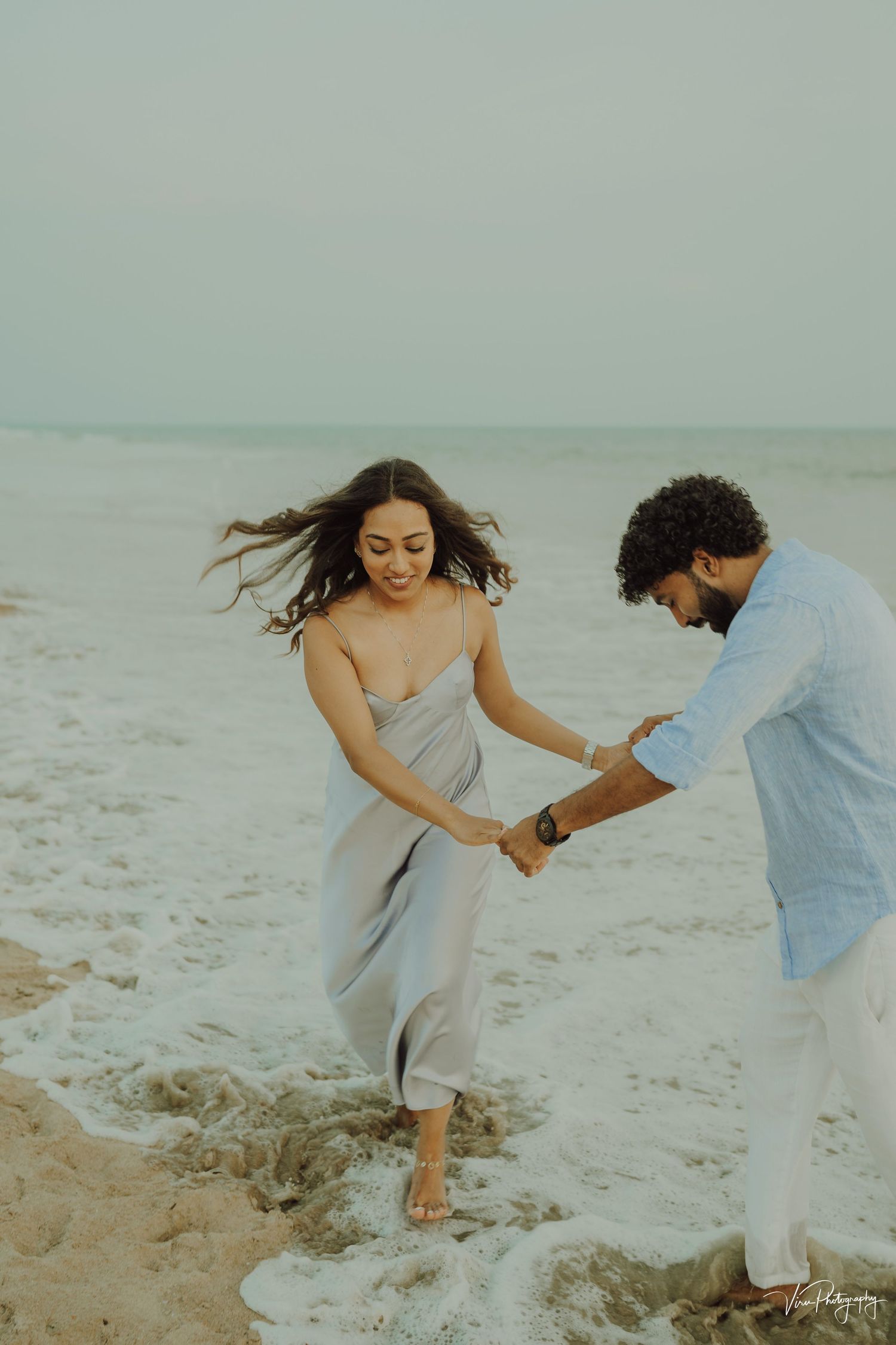 A couple holds hands while playing in the surf at the beach during golden hour.