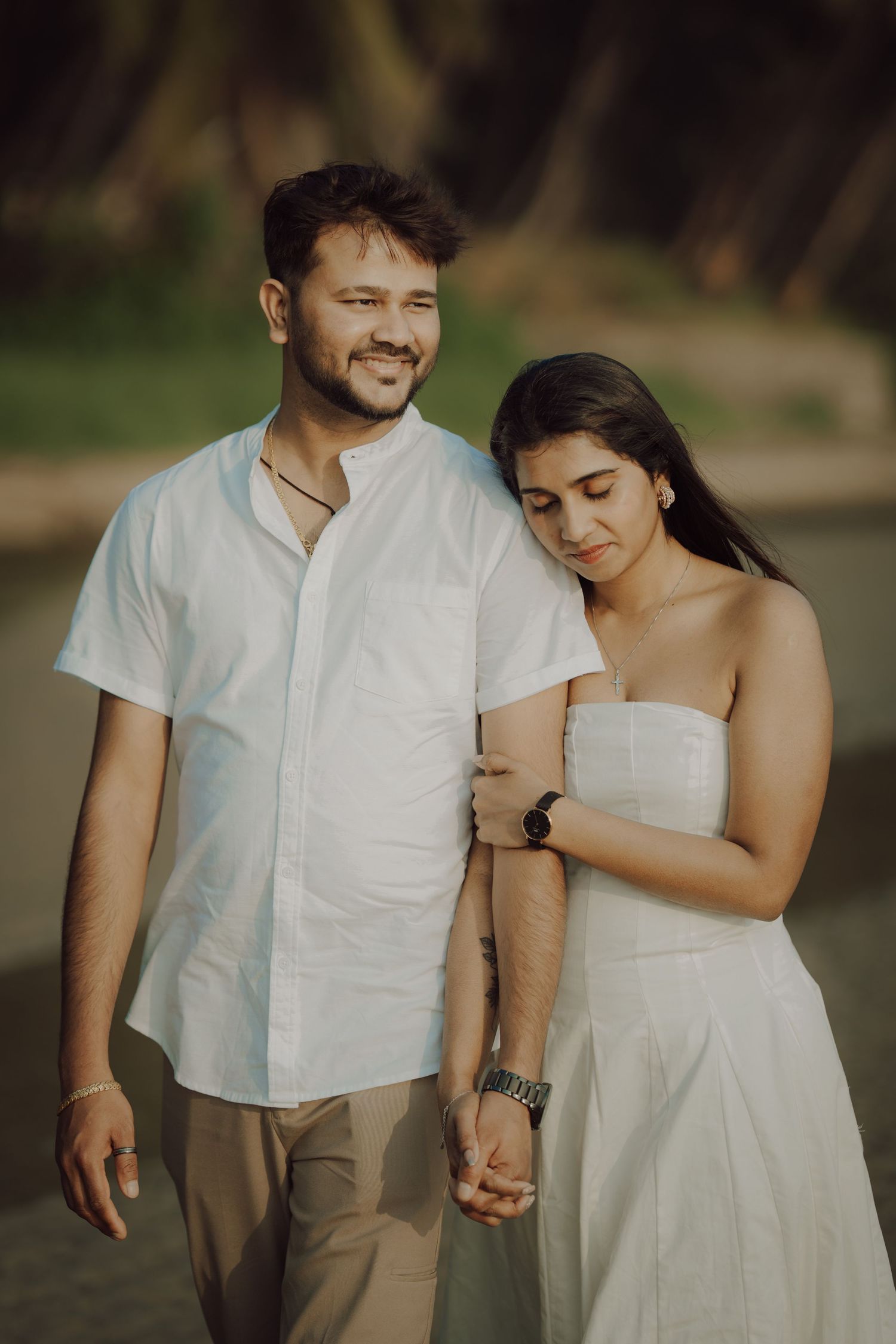 A couple in white and beige outfits share tender moments together during an outdoor photoshoot in a natural setting.