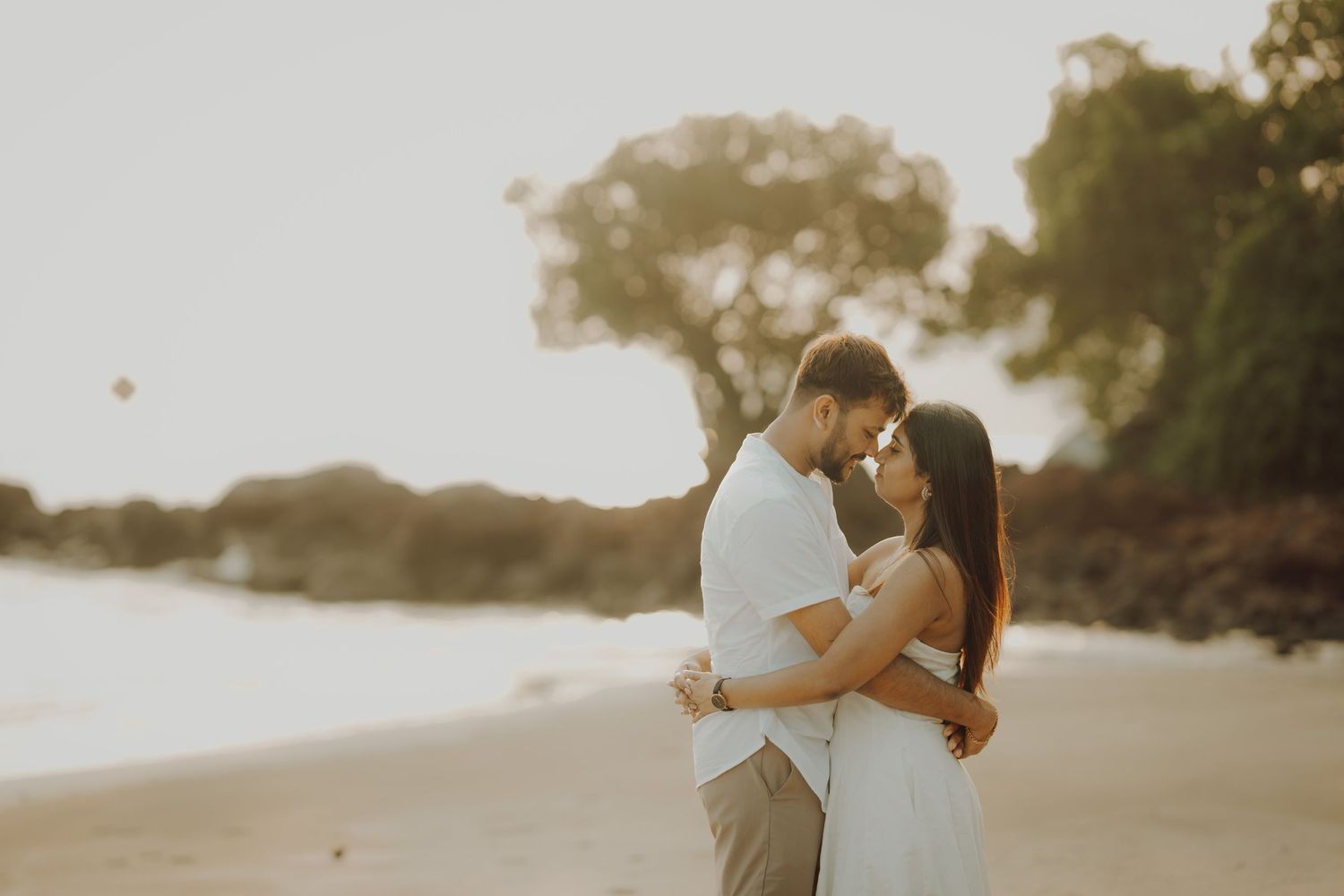 A romantic couple embraces on a misty beach at sunset during an intimate photoshoot.