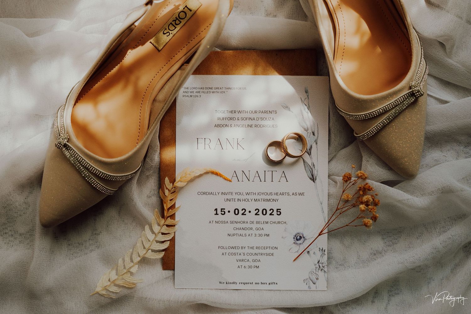 Wedding invitation card with golden wedding rings and beige bridal shoes on white fabric background.
