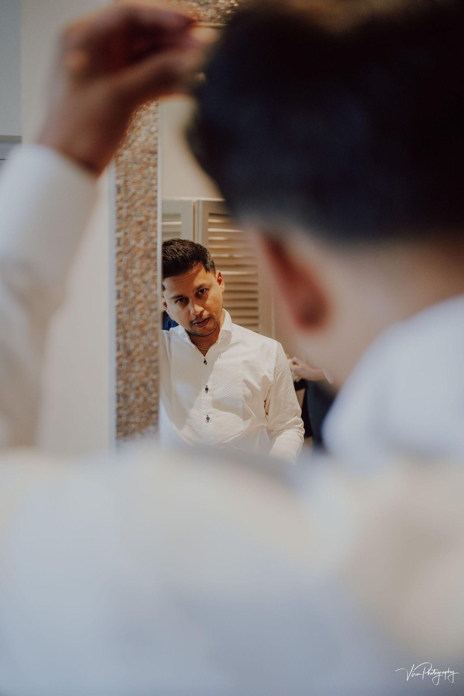 Someone looks in a mirror while getting ready, wearing a crisp white button-up shirt in an elegant setting.