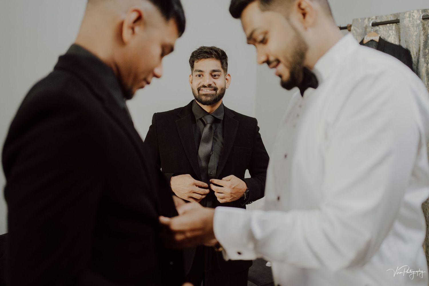 Three people in formal attire share a lighthearted moment together during what appears to be a wedding or special event.