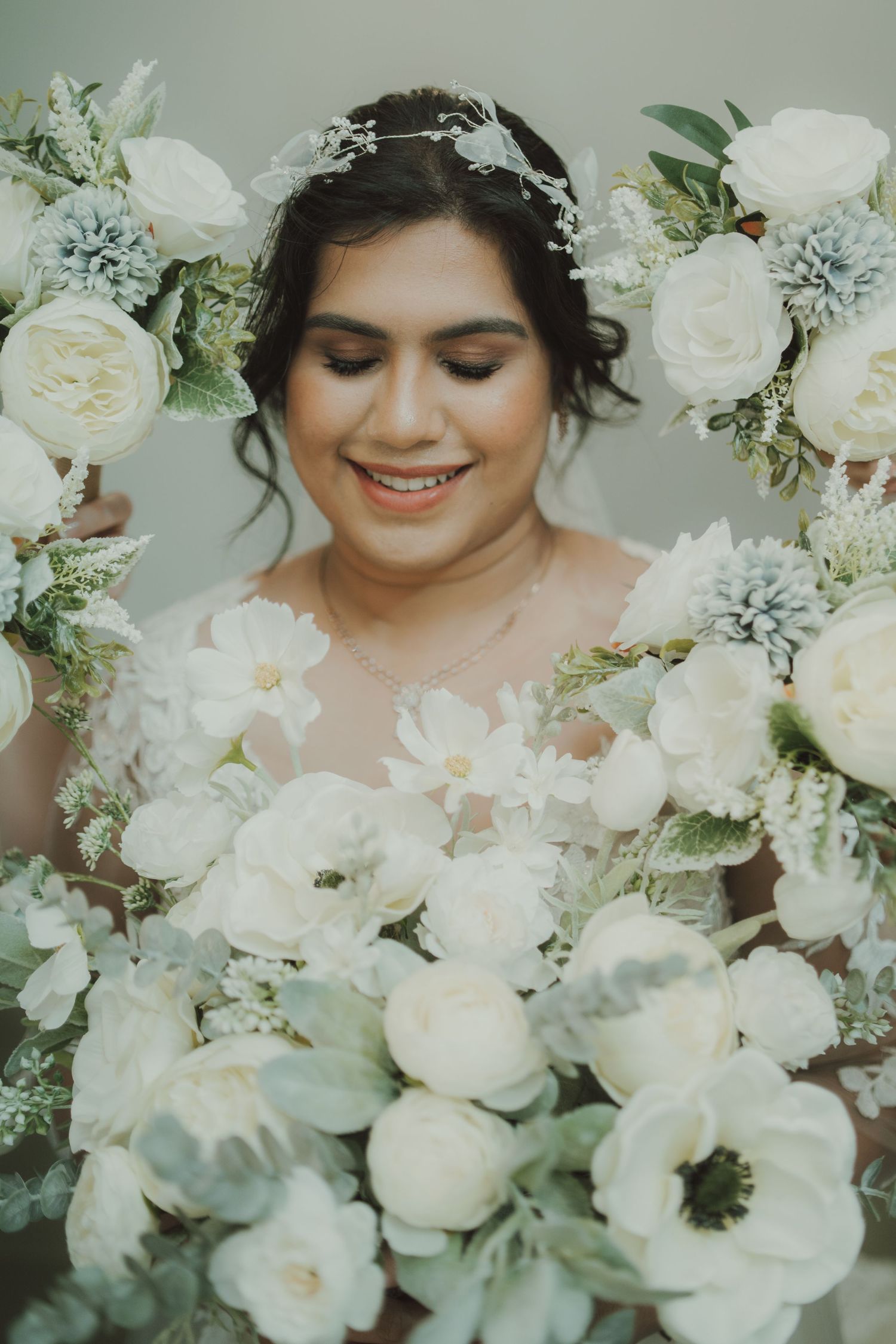Bride surrounded by white roses and soft blue flowers smiles with eyes closed.