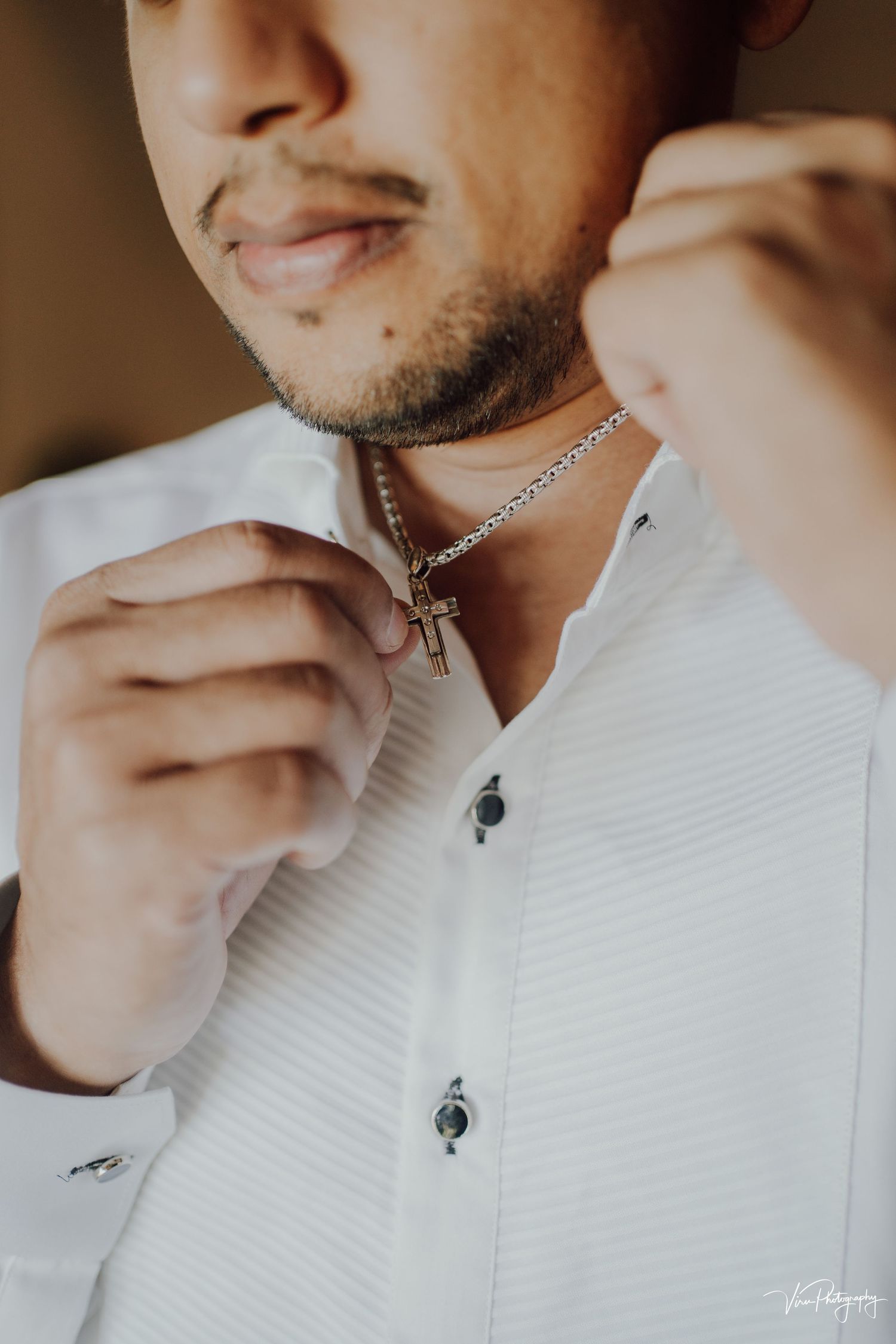 Close-up shot of someone wearing a white textured shirt and silver chain necklace in warm lighting.