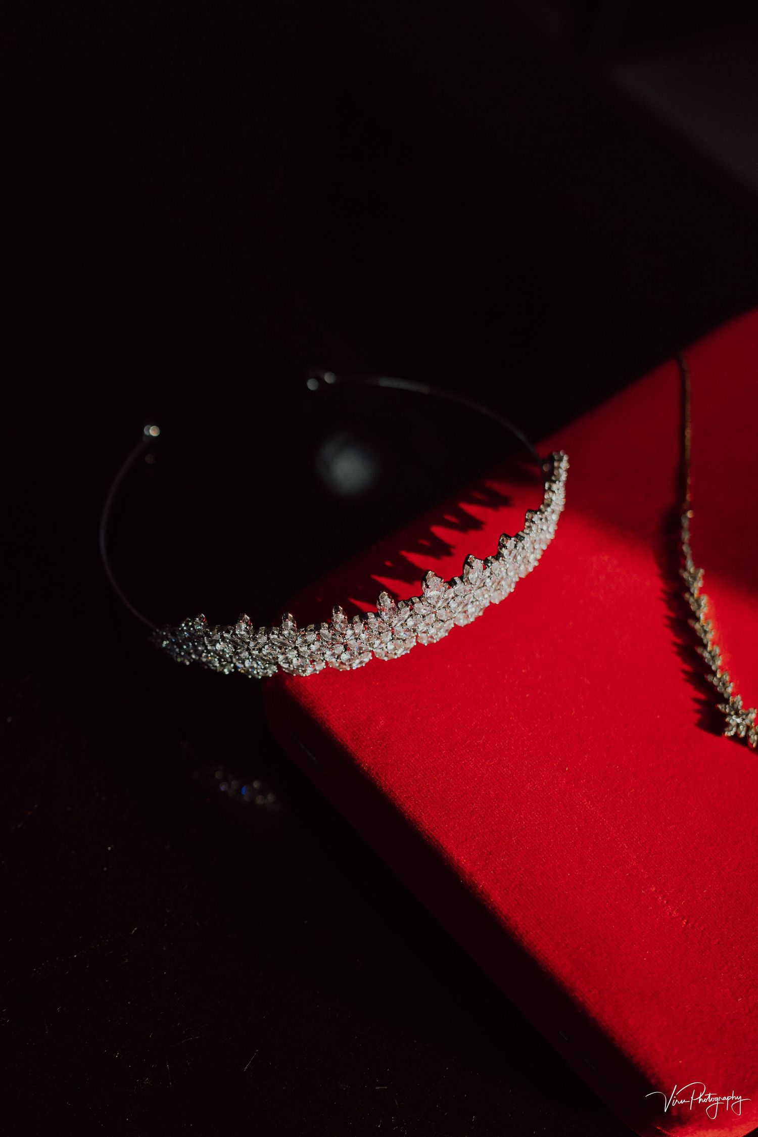 A delicate silver tiara with crystal embellishments rests on a red velvet surface in dramatic lighting.