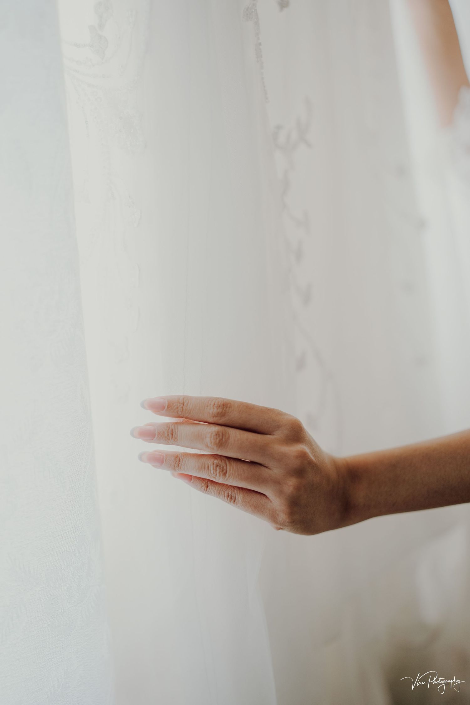 A delicate hand gently touches white fabric or curtain material in soft lighting.