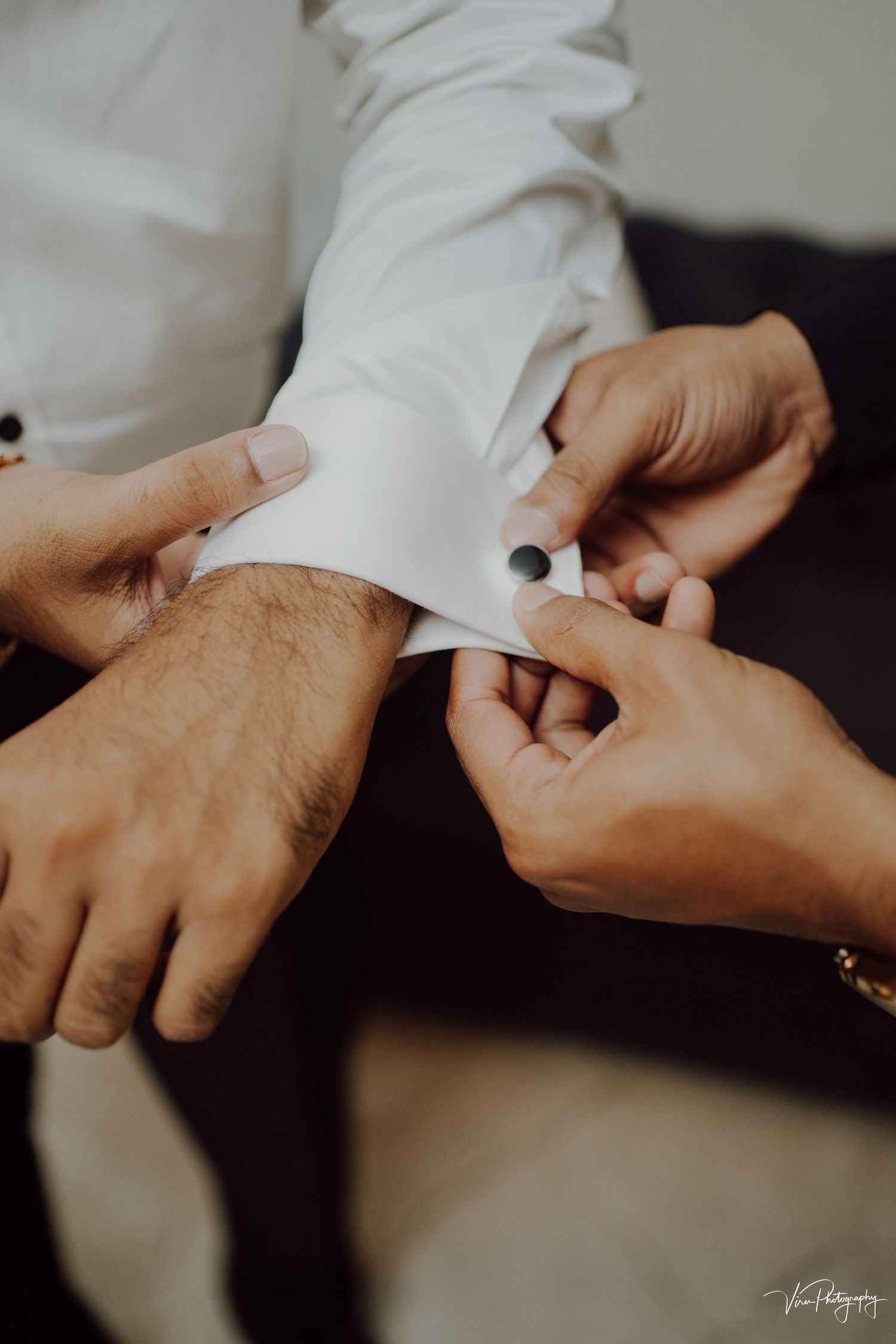 Close-up shot of hands buttoning a white dress shirt sleeve cuff in elegant wedding preparation.