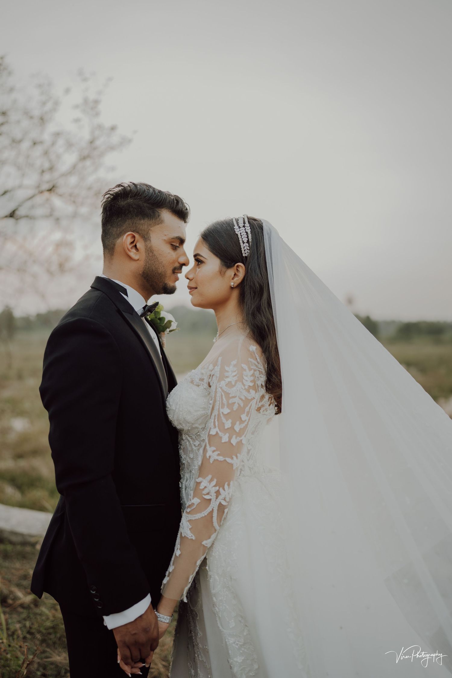 A couple in elegant wedding attire share an intimate moment outdoors with soft cherry blossoms in the background.