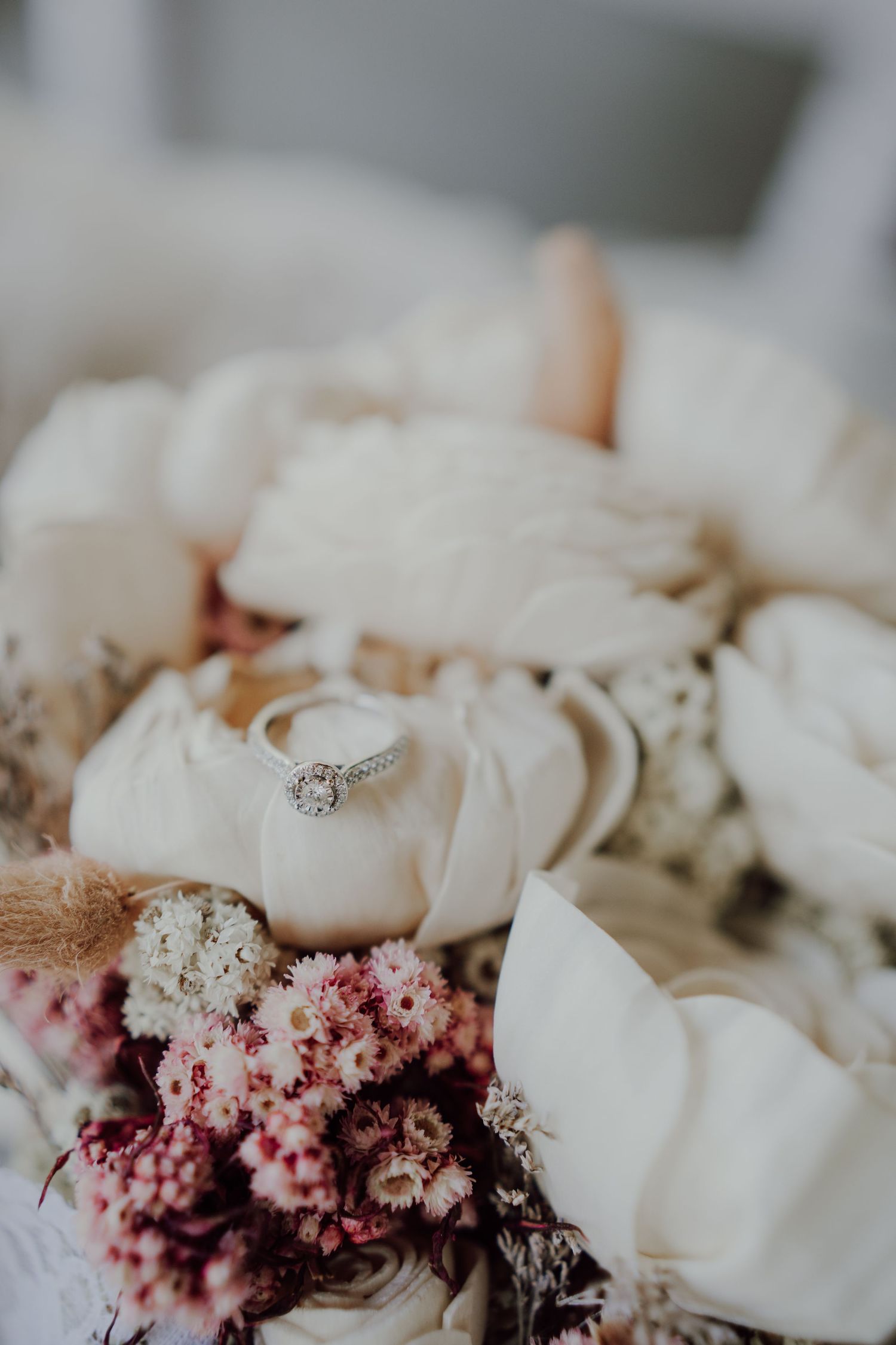 A sparkling diamond engagement ring nestled among white and pink floral arrangements.