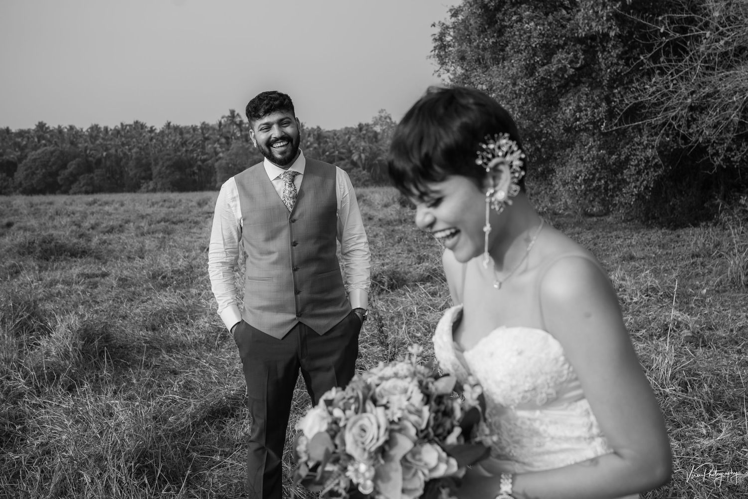 Black and white wedding photo of a couple outdoors in a field, with the bride holding a floral bouquet.