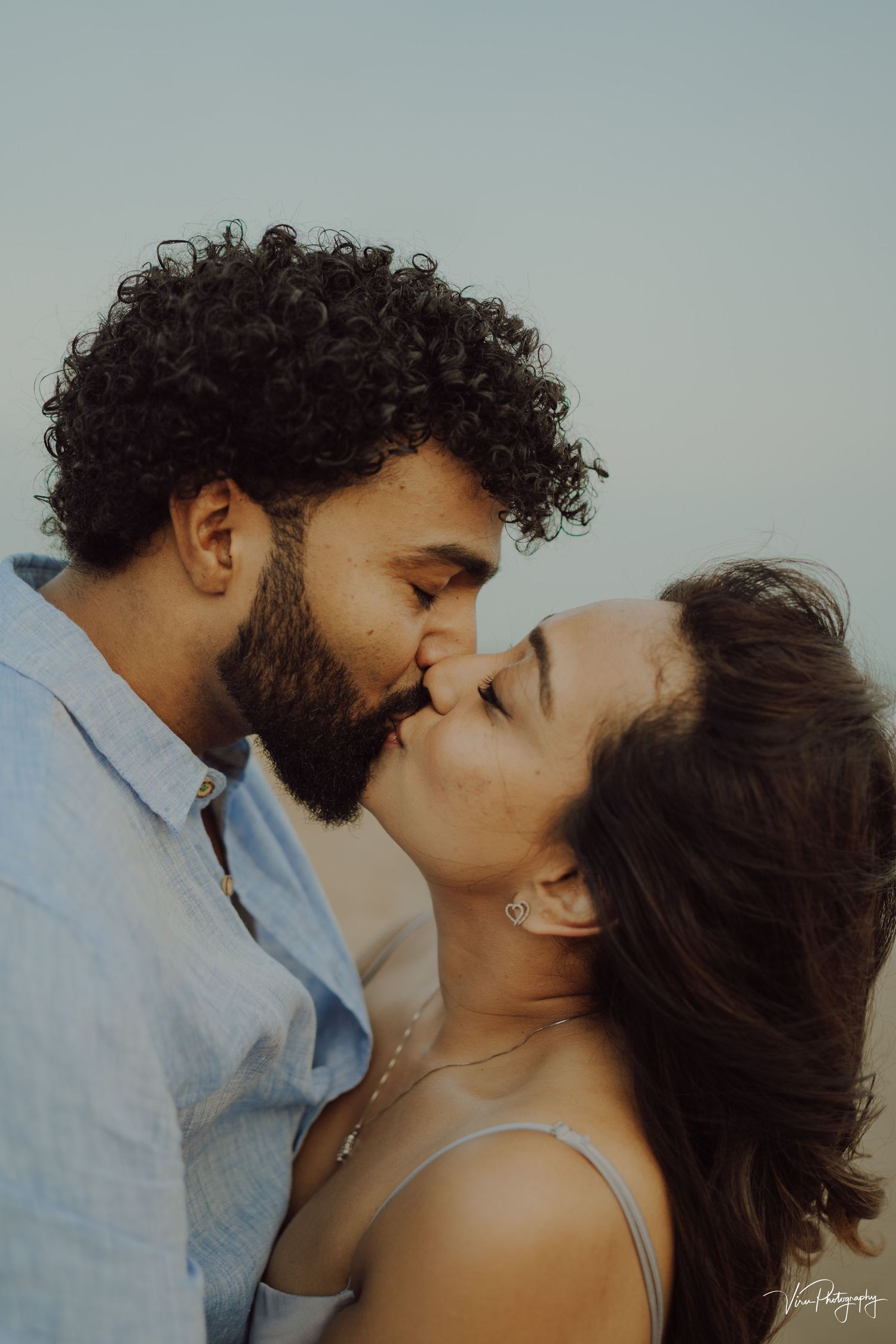 A tender romantic moment captured between a couple sharing a kiss during a dreamy outdoor photo session.