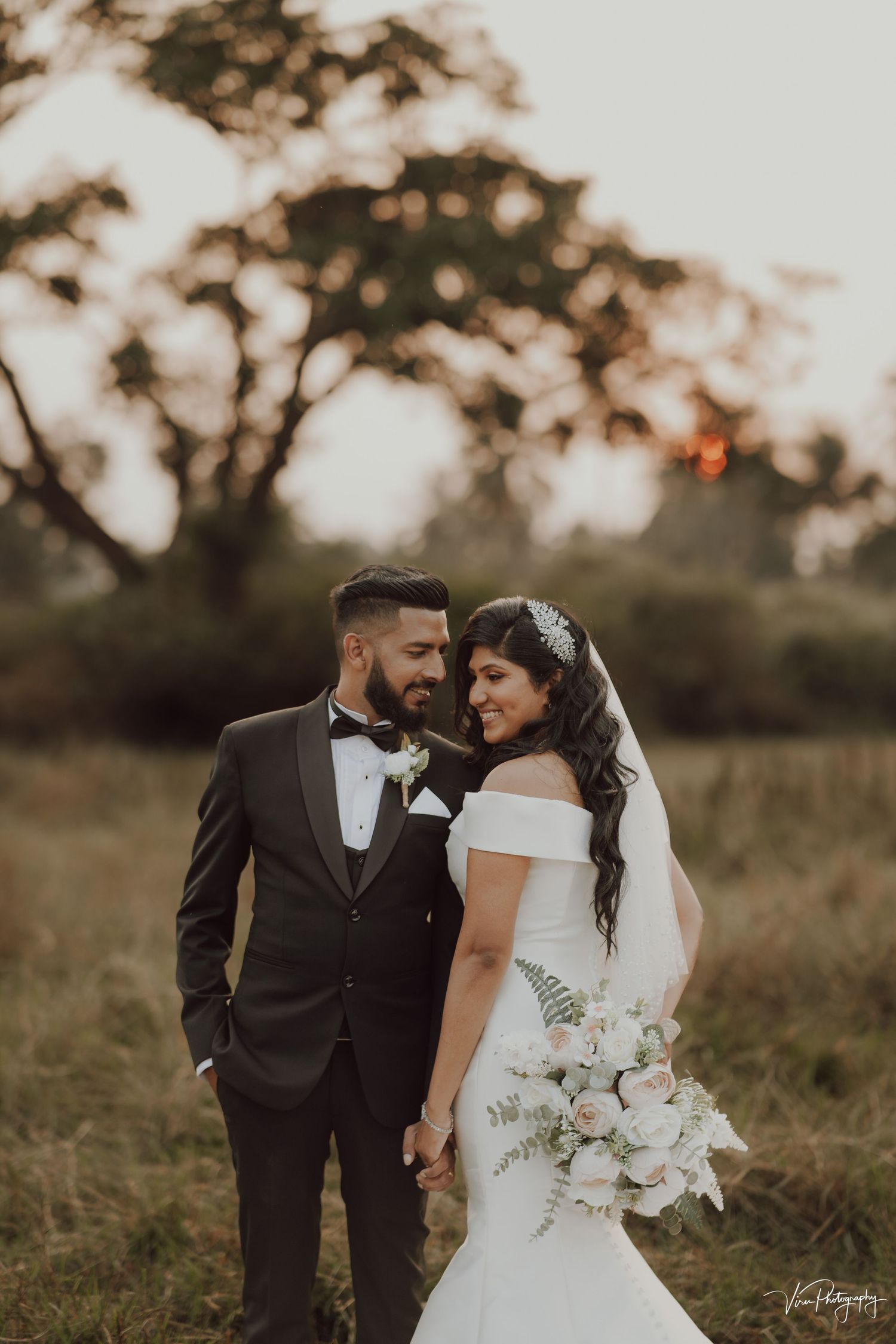 A romantic sunset wedding portrait shows a couple in a natural field setting with the bride holding a beautiful bouquet.