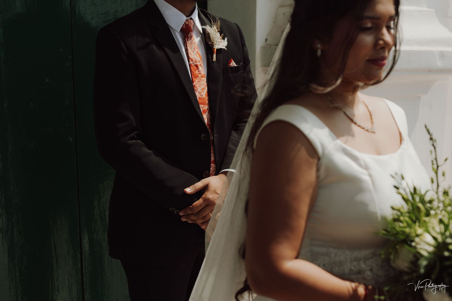 Wedding photograph showing couple in traditional attire with bride in white dress holding bouquet against moody lighting.