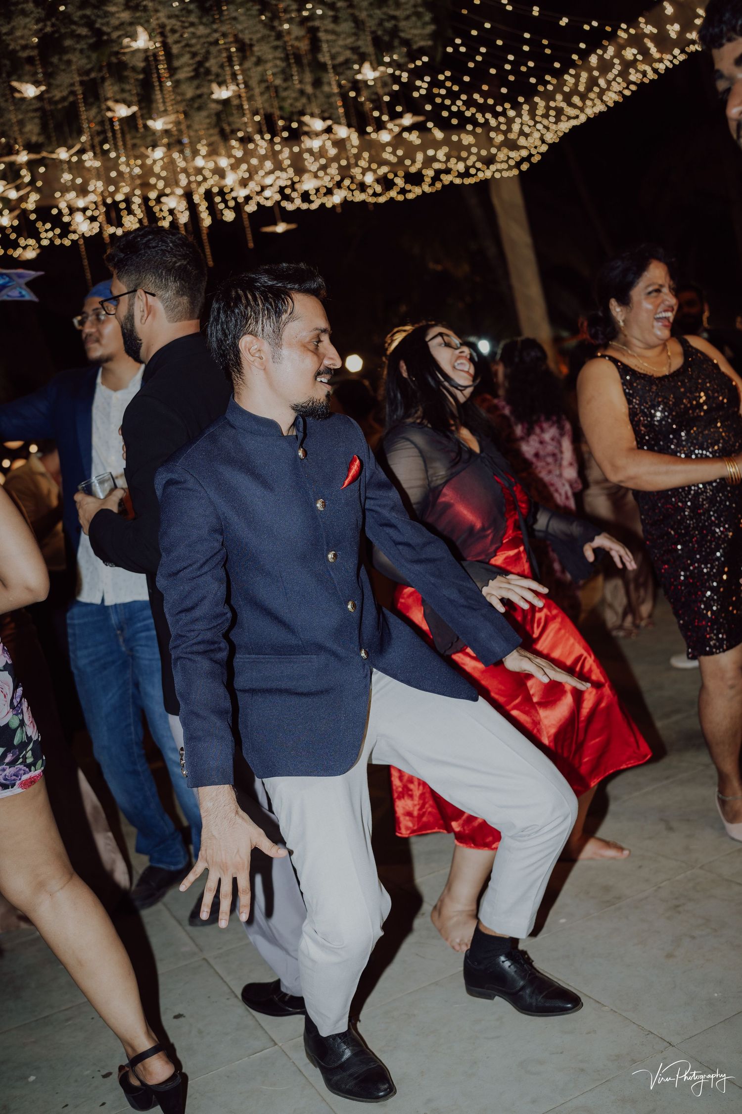 Party guests dance beneath twinkling string lights at an evening celebration with sparkling decor.
