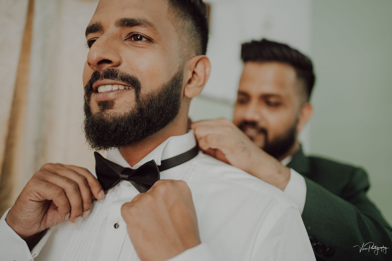 Someone helps adjust a black bow tie on a person wearing a crisp white dress shirt during formal preparation.