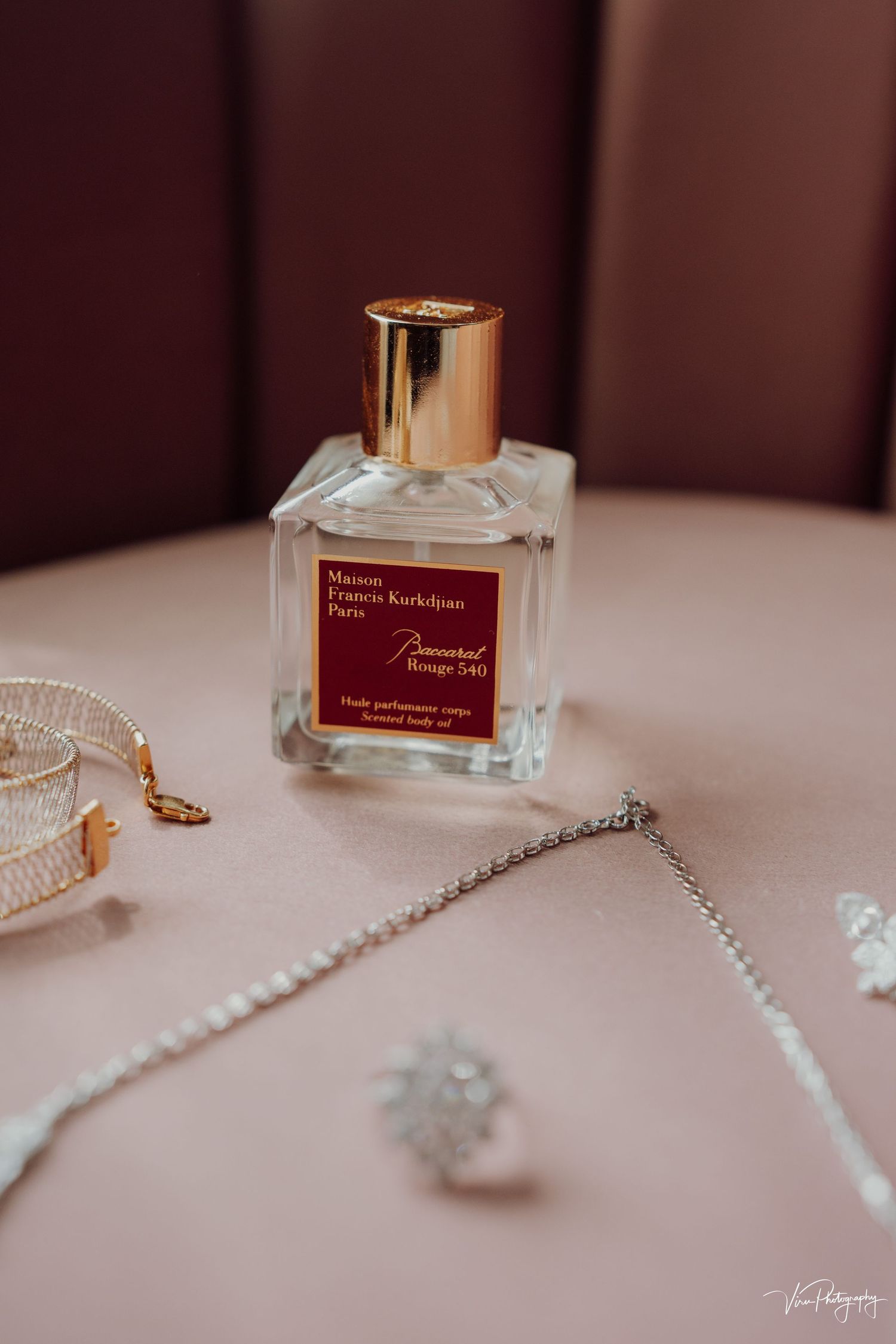 Luxury perfume bottle with gold cap sits elegantly on pink surface beside delicate pearl necklace and jewelry.