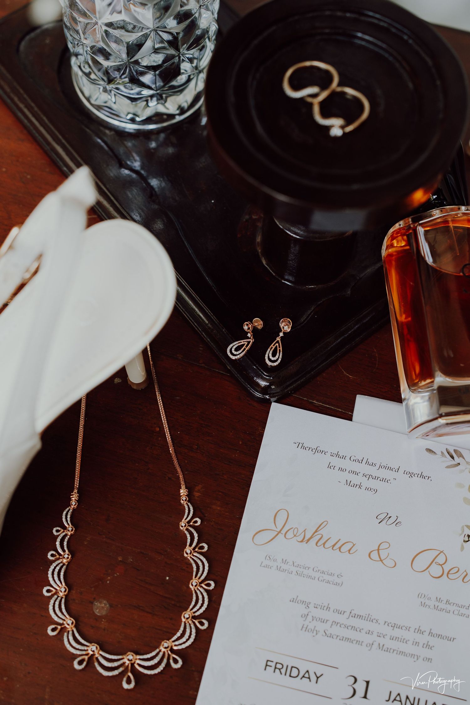 Wedding details including jewelry, invitation, rings, and decor arranged on a wooden surface create an elegant flat lay.