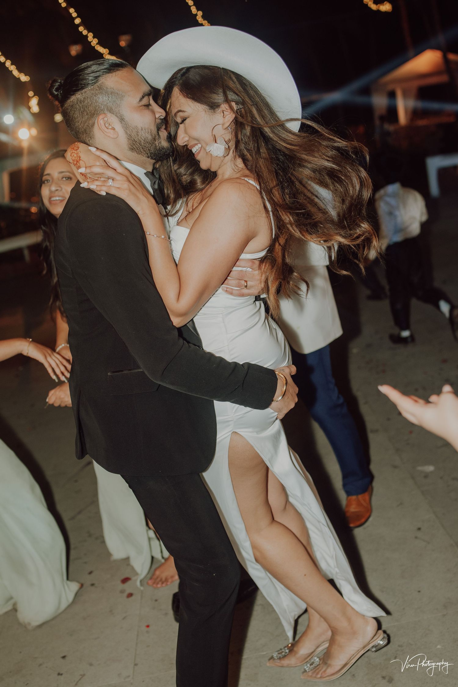 A couple dances intimately at a nighttime wedding reception as a white dress swirls in the soft lighting.