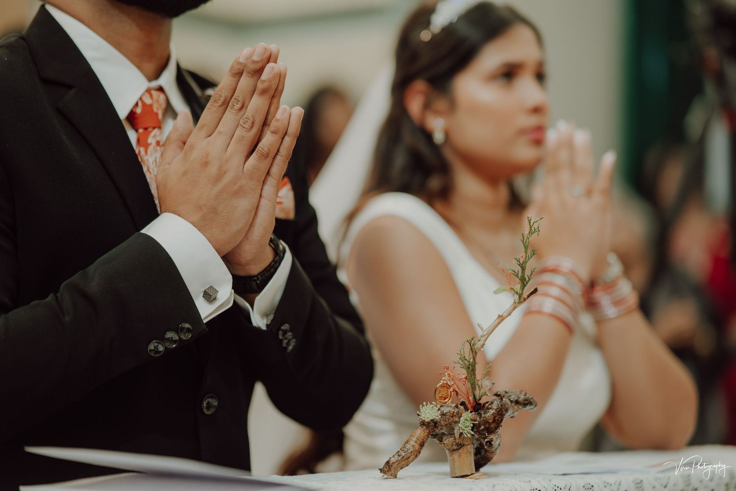 Couple in formal wedding attire praying together at a decorated ceremony table.